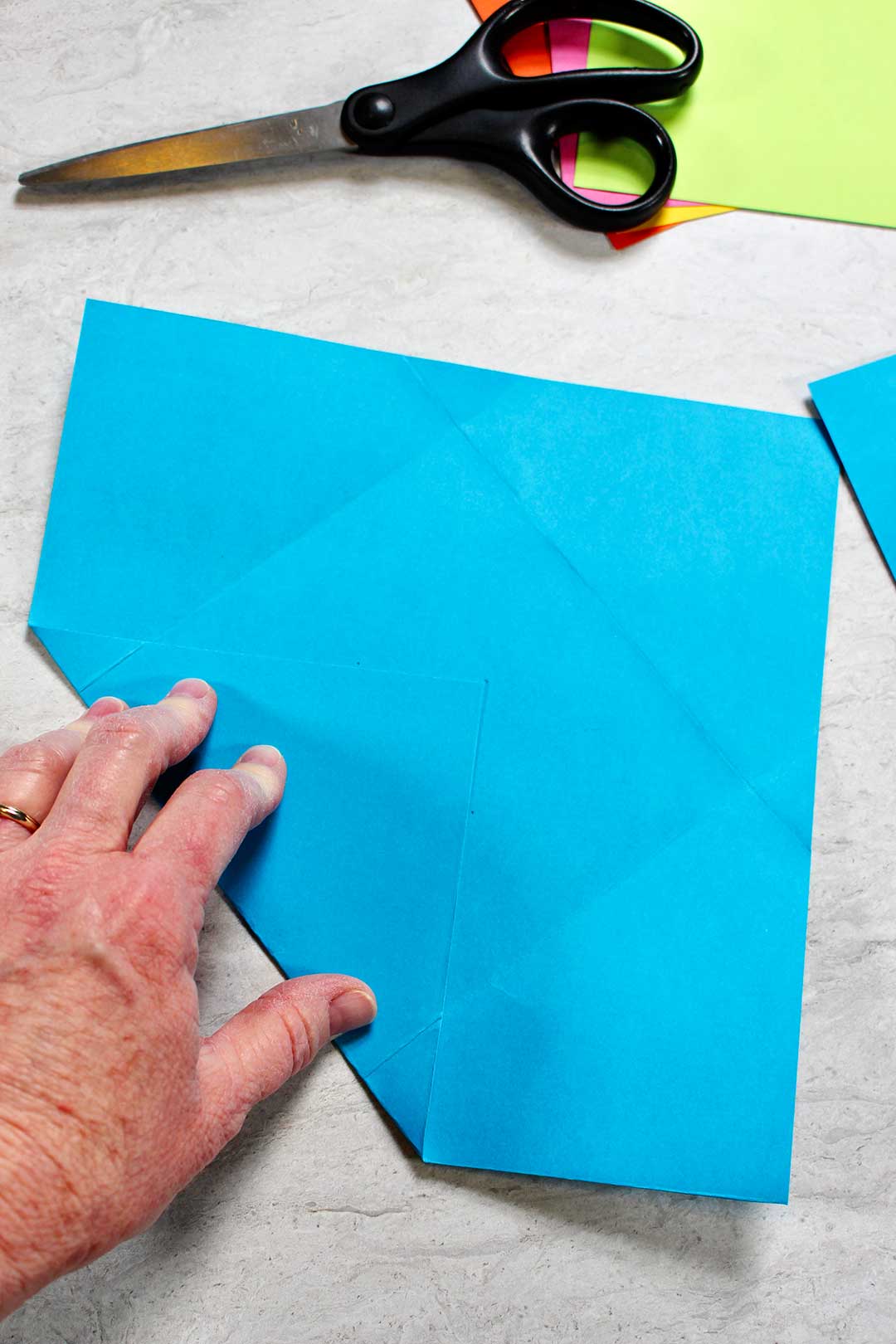 Folding a corner of a blue square of paper to make a homemade envelope.