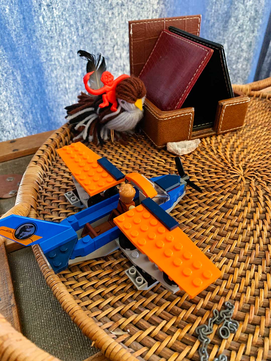 A lego airplane, a plastic monkey, and a yarn bird sitting on a side table.