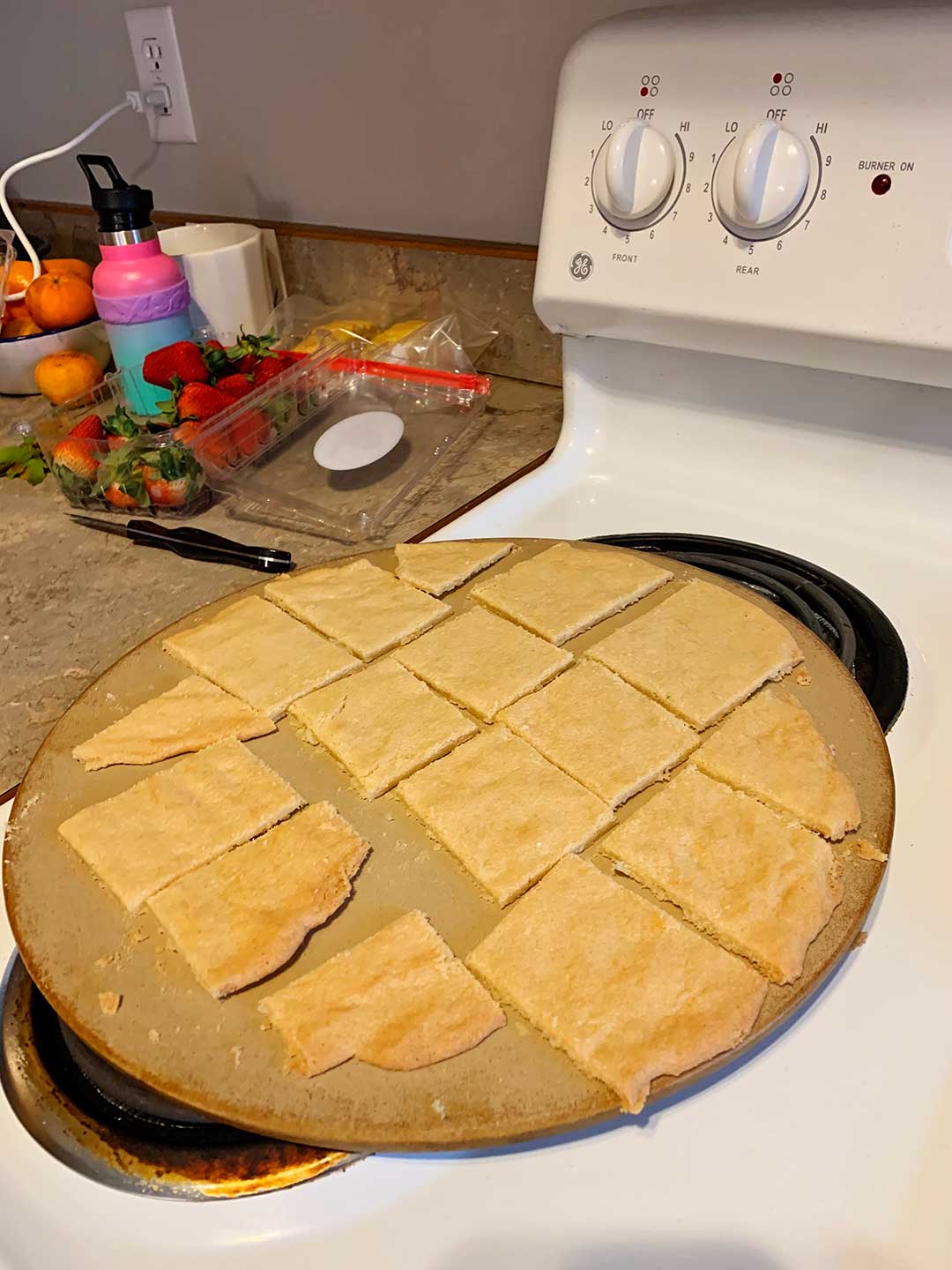 A sugar cookie crust on a pizza stone, sitting on the oven near some strawberries.
