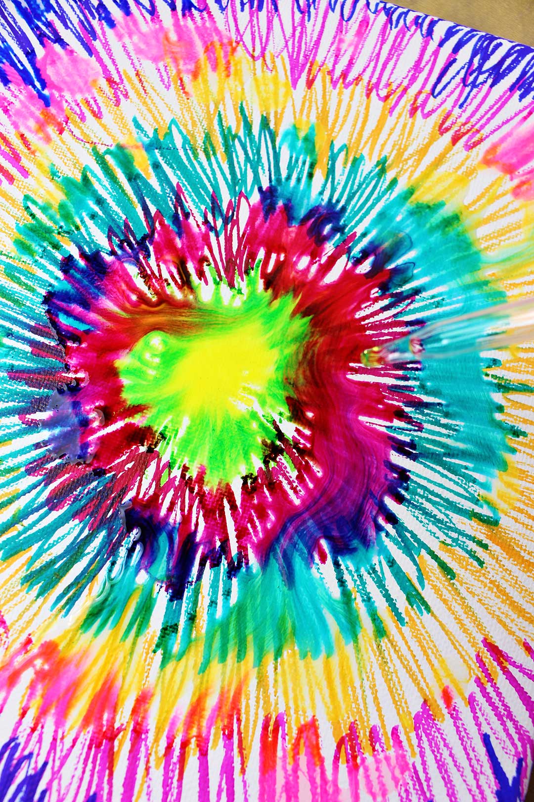 A canvas colored with sharpies in a tie dye pattern, beginning to swirl from drops of alcohol..