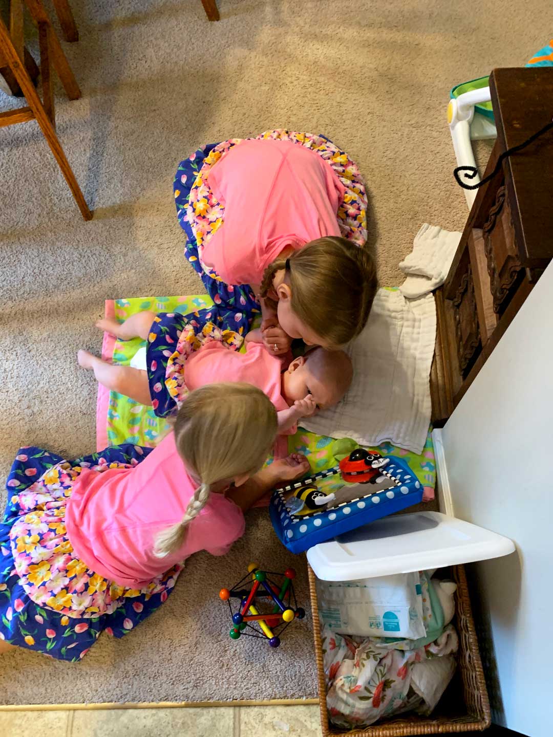 Two girls gathered around a baby, all wearing pink and floral homemade t-shirt dresses.