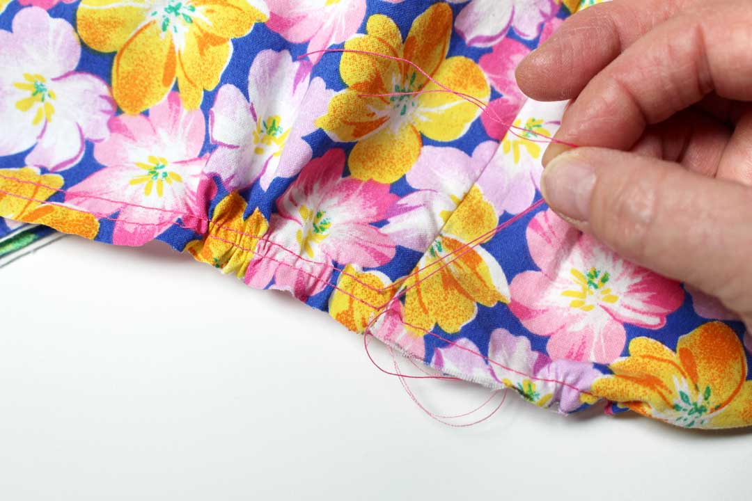 A hand pulling two strings to gather floral patterned fabric together. 