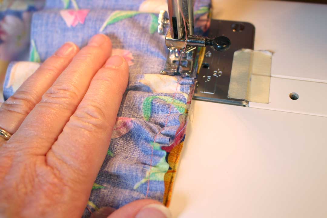 Someone sewing several layers of floral fabric together on a sewing machine. 