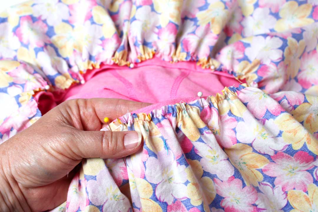 Straight pins holding gathered floral fabric to a pink tshirt edge before sewing together a t-shirt dress.