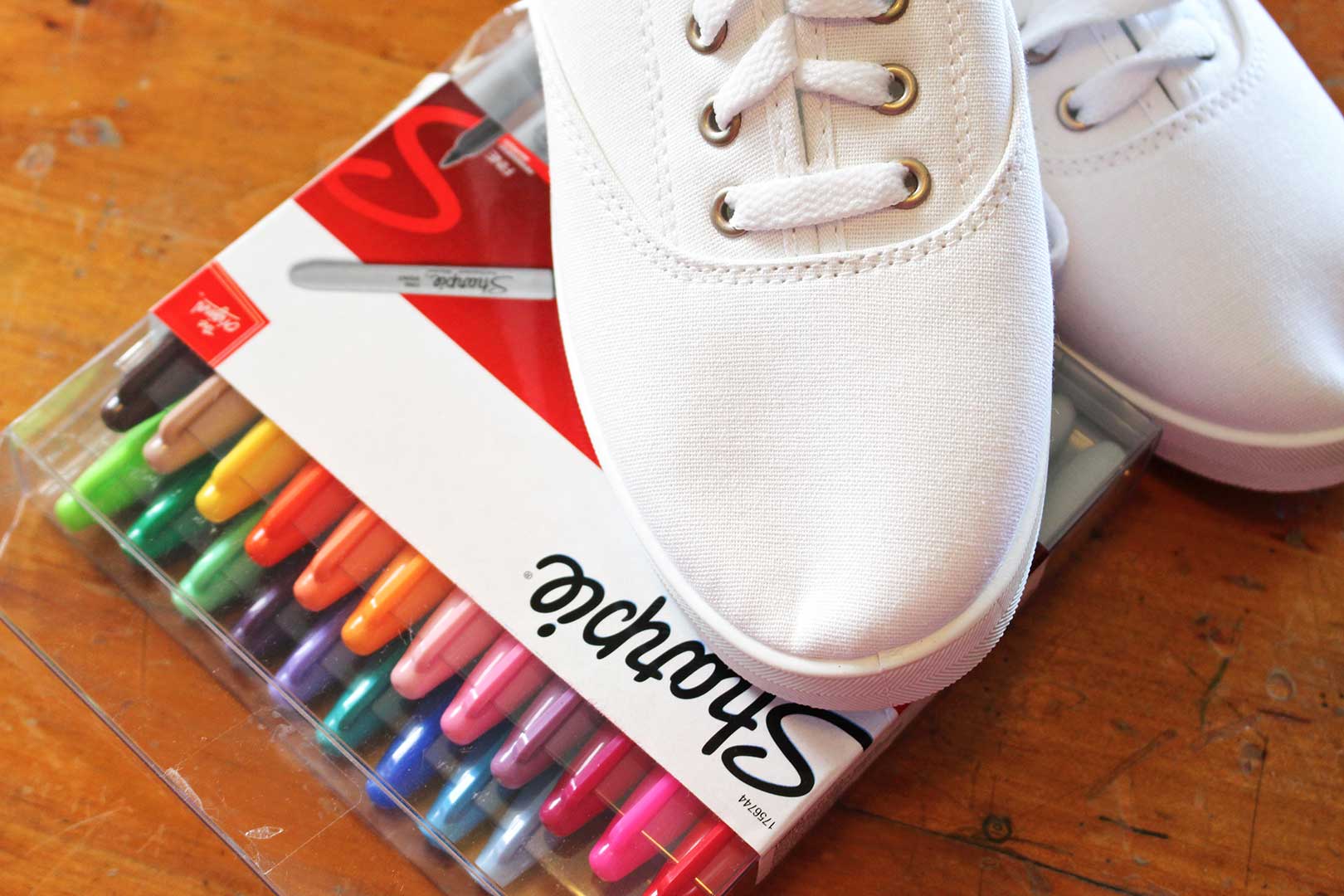 A pair of white canvas shoes and some colorful Sharpie markers.