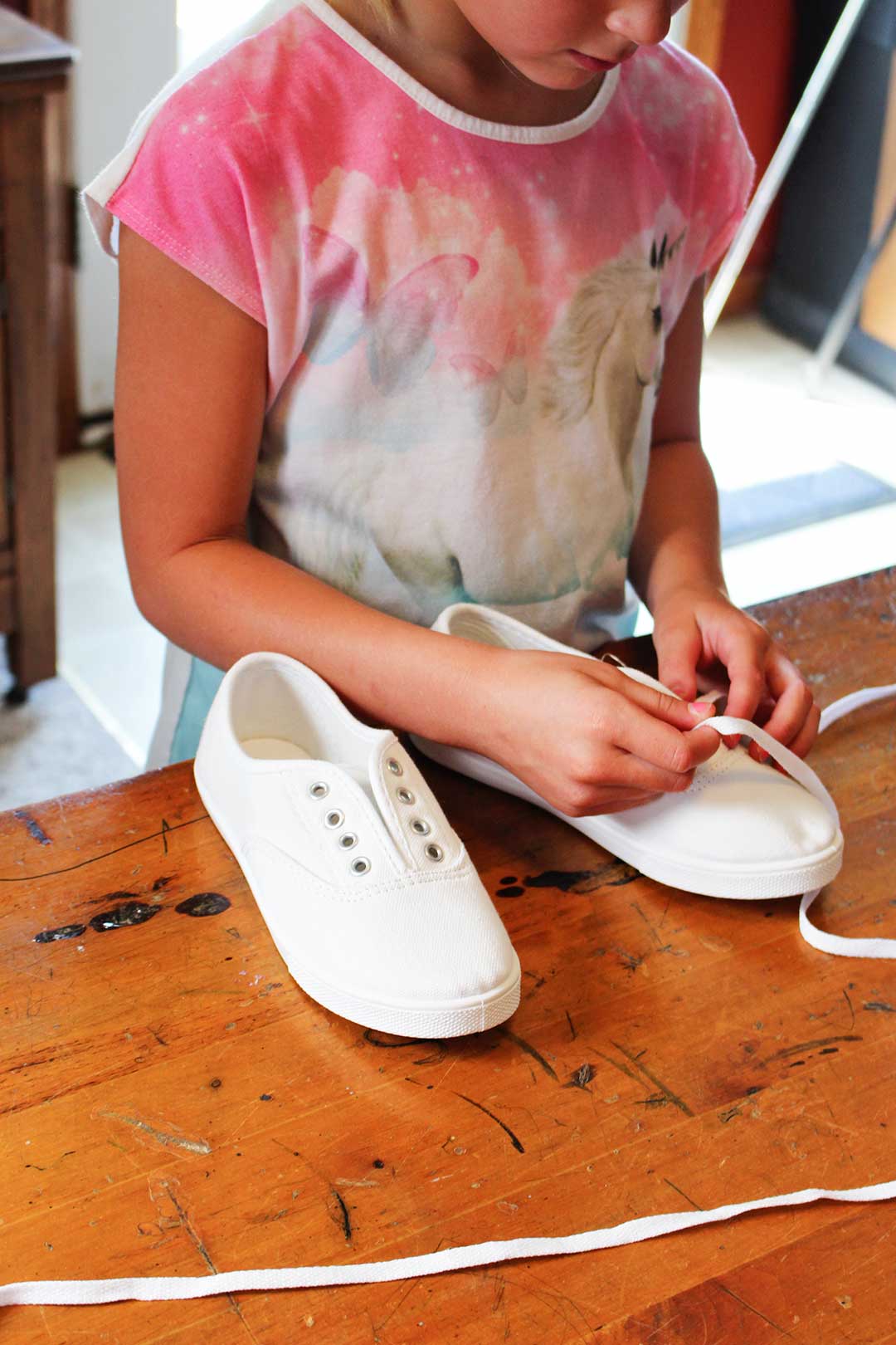 A child adding shoelaces to a pair of white canvas shoes.