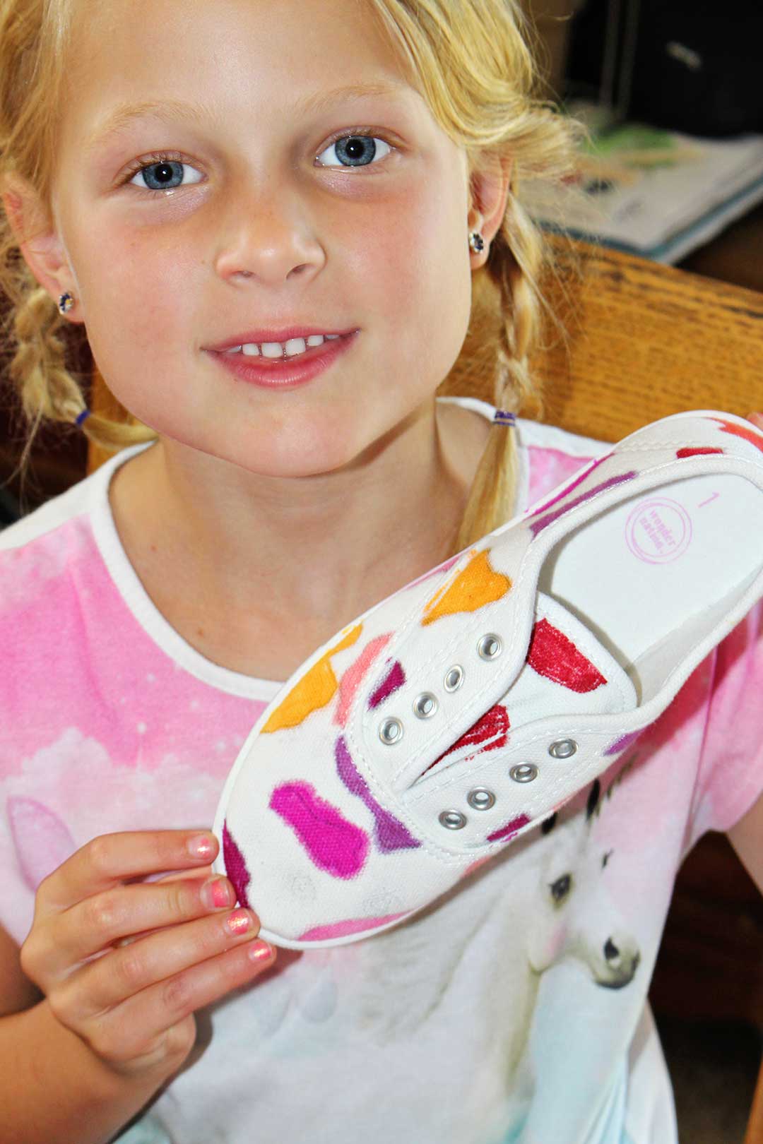 A child holding a canvas shoe decorated with colorful markers.