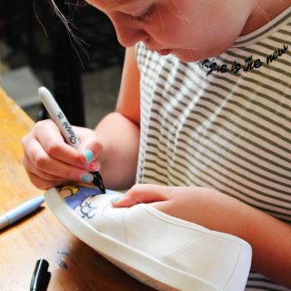 A child coloring on a white canvas shoe with a marker.