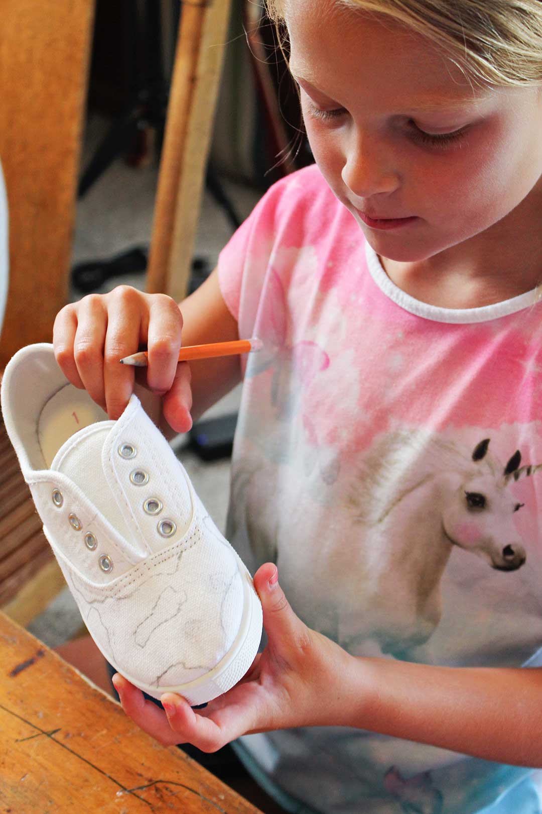 A child drawing with a pencil on a white canvas shoe.