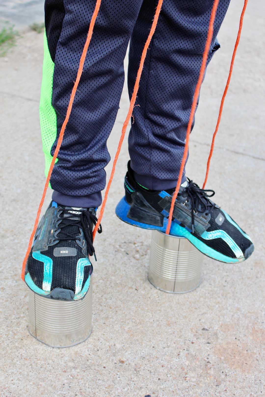 A child in tennis shoes stepping on recycled tin can stilts.