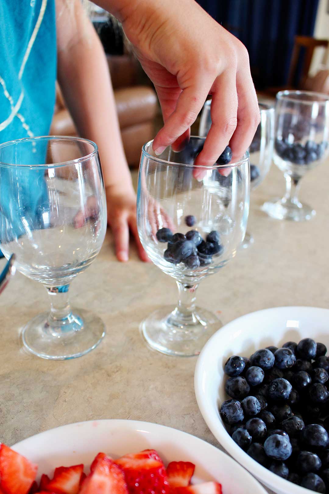 A child adding blueberries to a glass parfait cup.