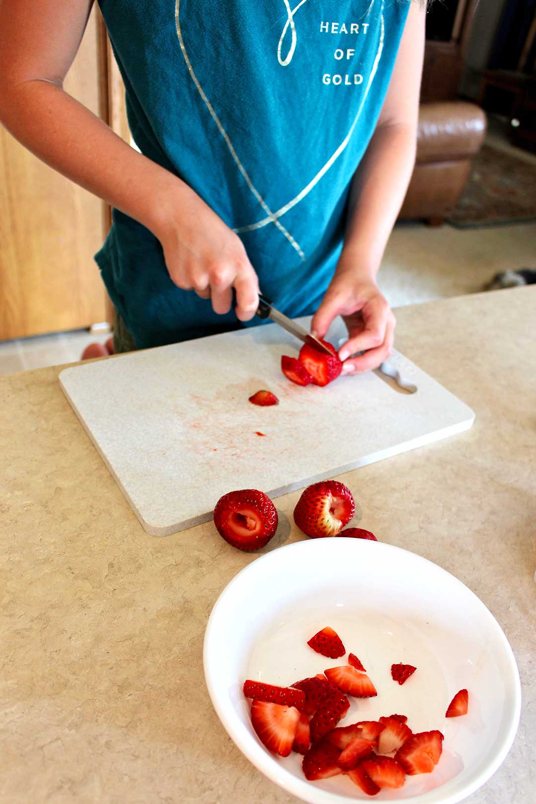 A child slicing strawberries on a cutting board.