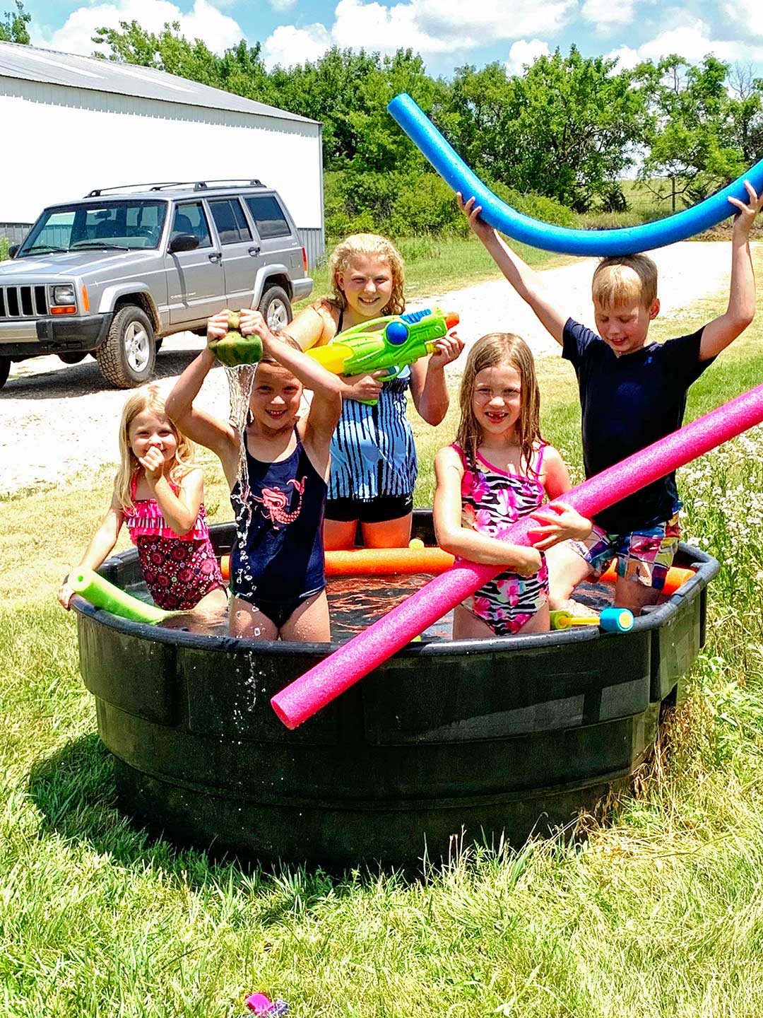 Kids swimming in a tank of water with squirt guns, noodles, and sponges.