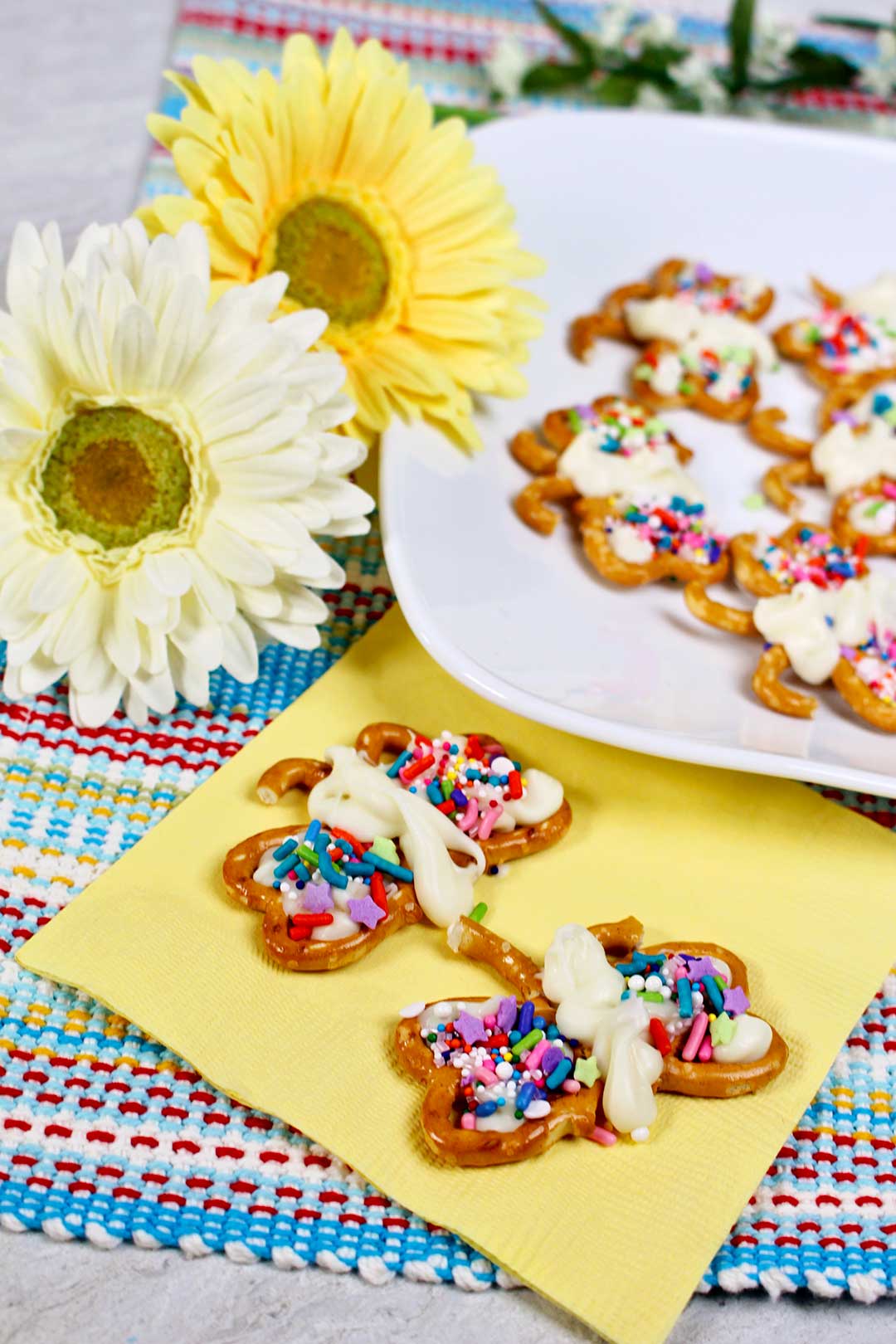 Colorful butterfly pretzel cookies decorated with sprinkles sitting next to daisies.