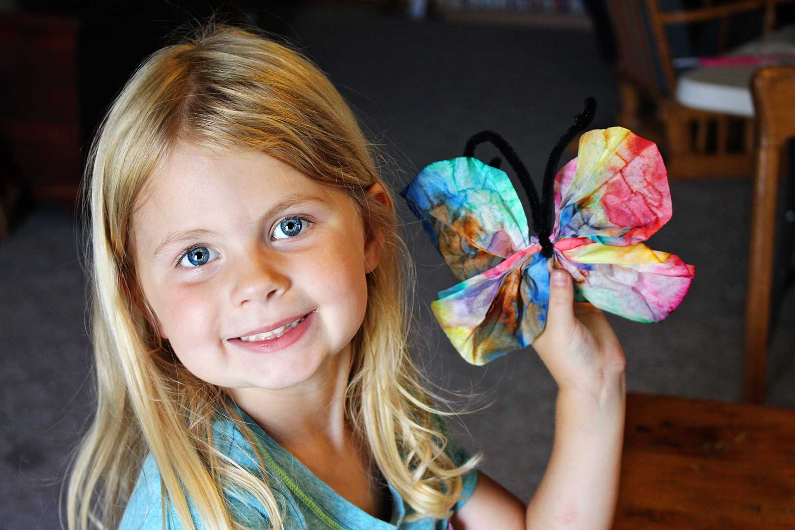 A child holding a colorful coffee filter butterfly craft.