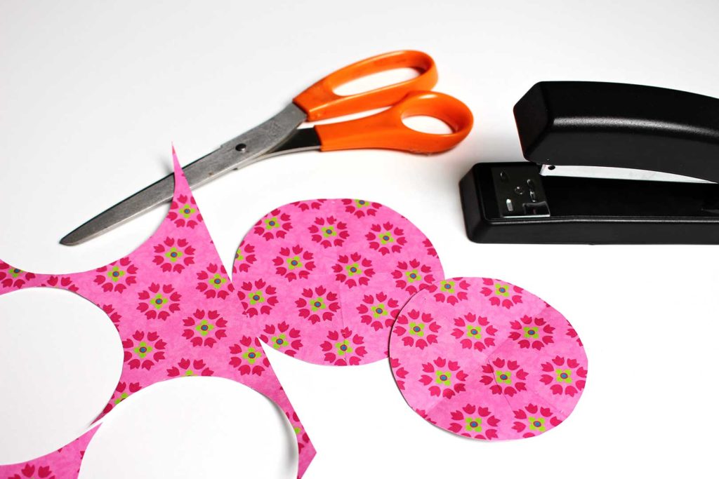 Two circles cut out of bright pink paper near a pair of scissors and a stapler.