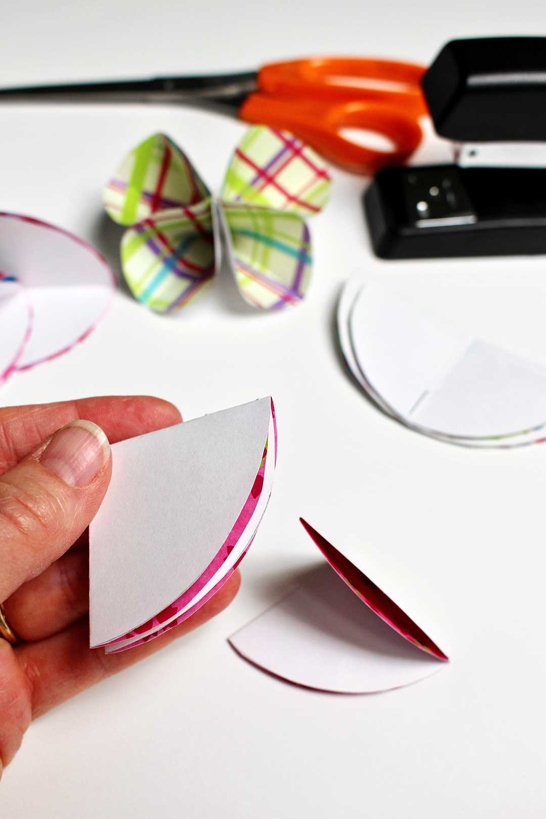 A circle of paper folded into quarters near a stapler and a pair of scissors.
