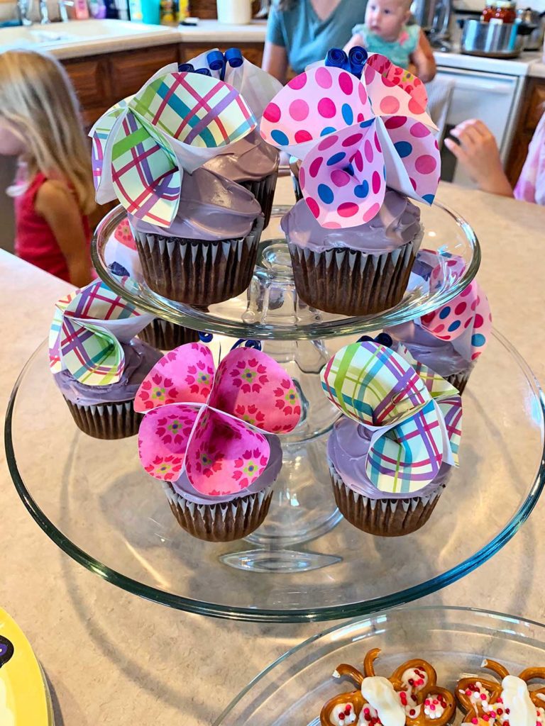 Un présentoir à gâteaux avec des cupcakes givrés violets, surmontés de décorations pour cupcakes papillons en papier DIY.