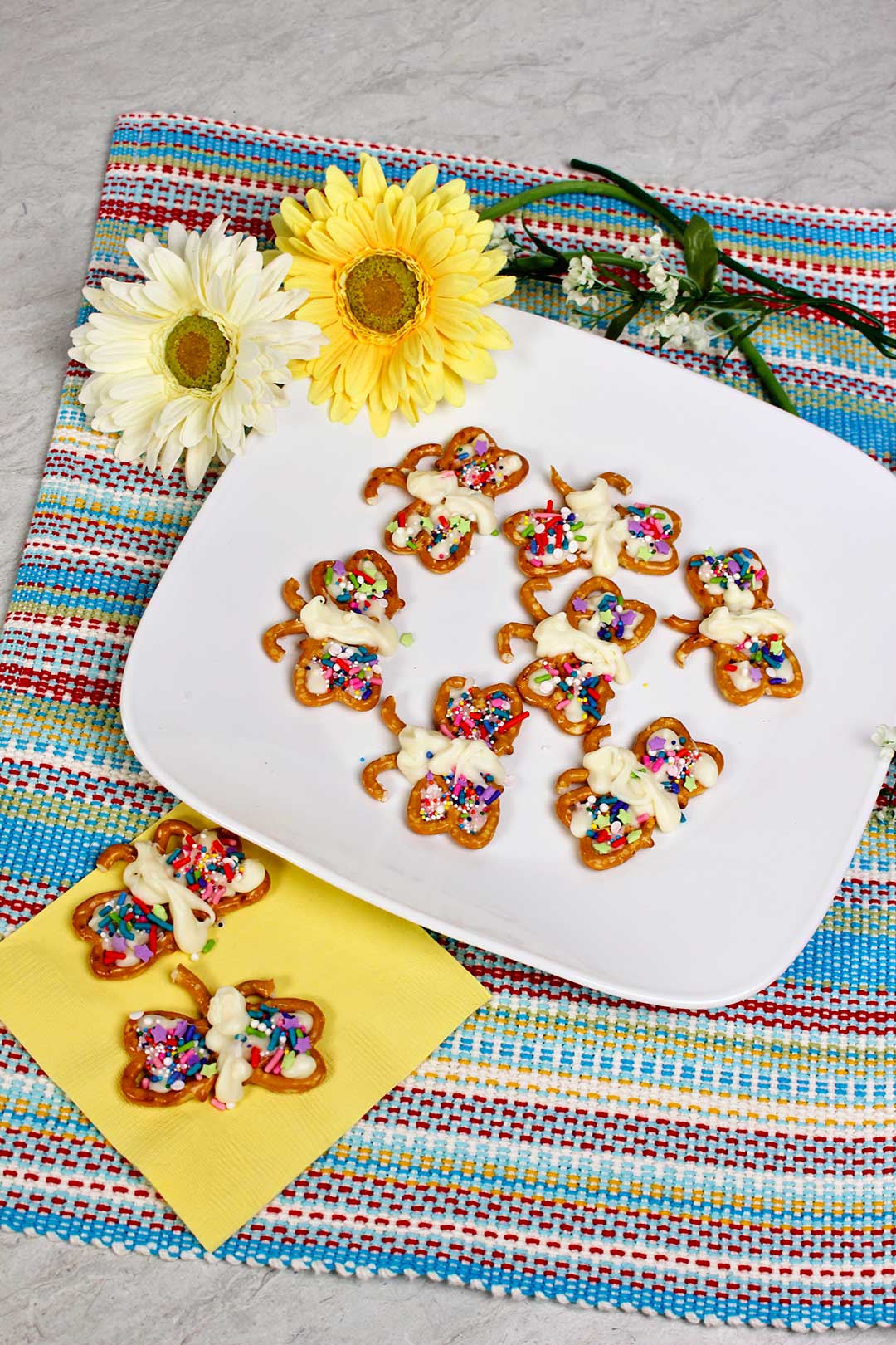 Decorated Butterfly Pretzel Cookies displayed on a yellow napkin near yellow flowers.