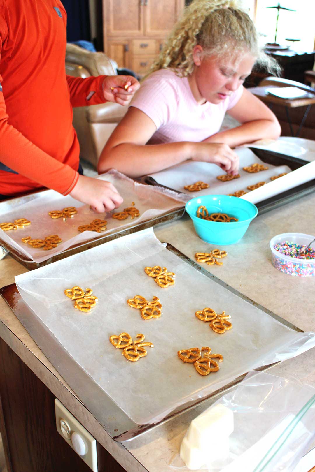 Children arranging pretzels in the shapes of butterflies on a trays covered with parchment paper.