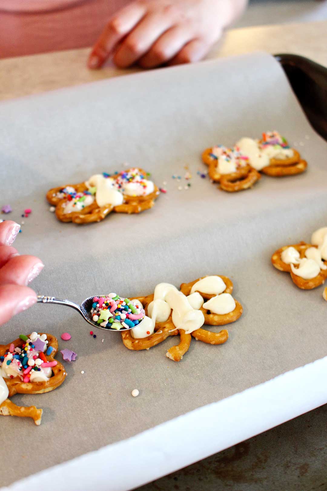 A child adding a spoonful of sprinkles to a Butterfly Pretzel Cookie.