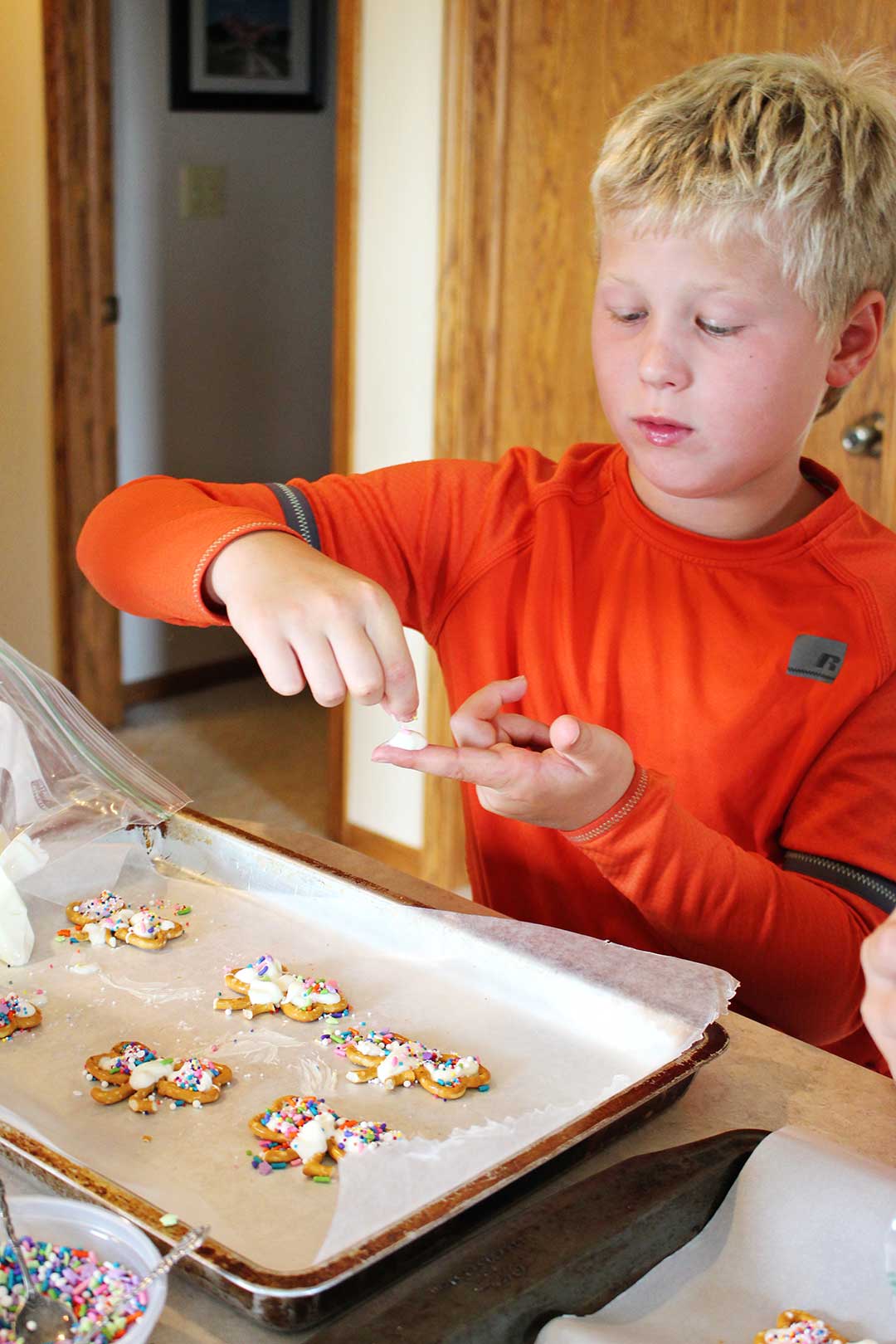 A child adding frosting to his finger while making pretzel cookies.