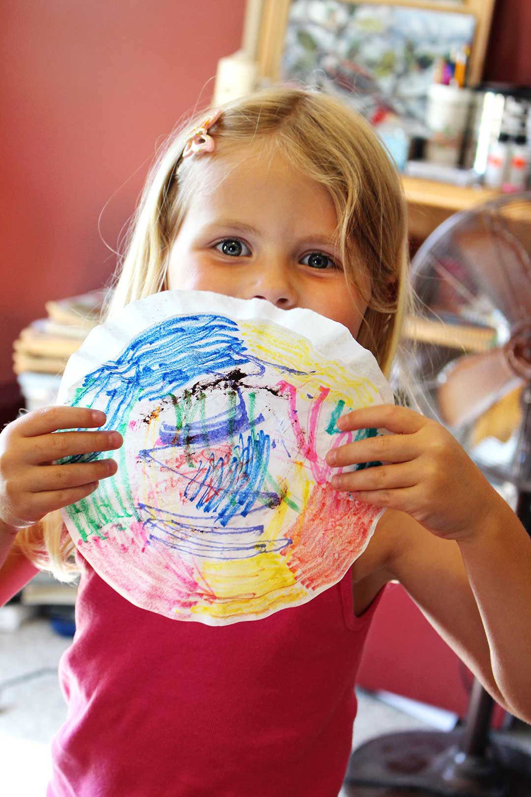 A child holding up a coffee filter colored with markers.