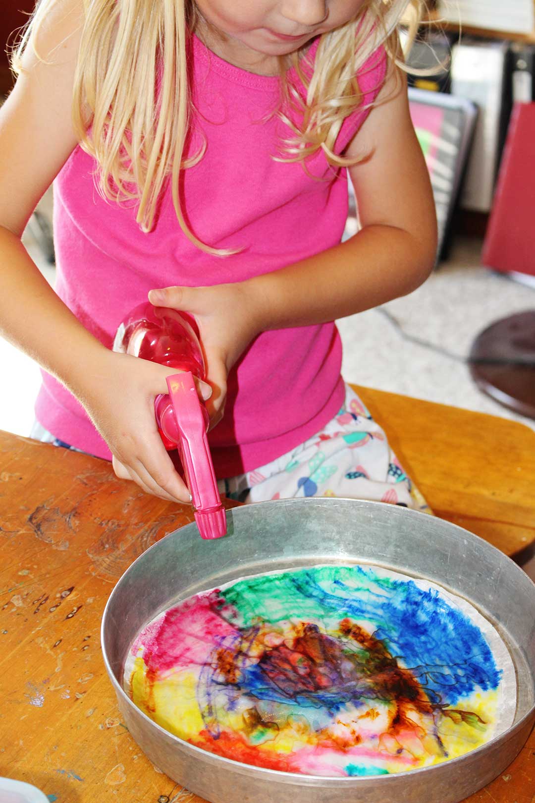 A child using a spray bottle to spray over her coffee filter colored with markers.