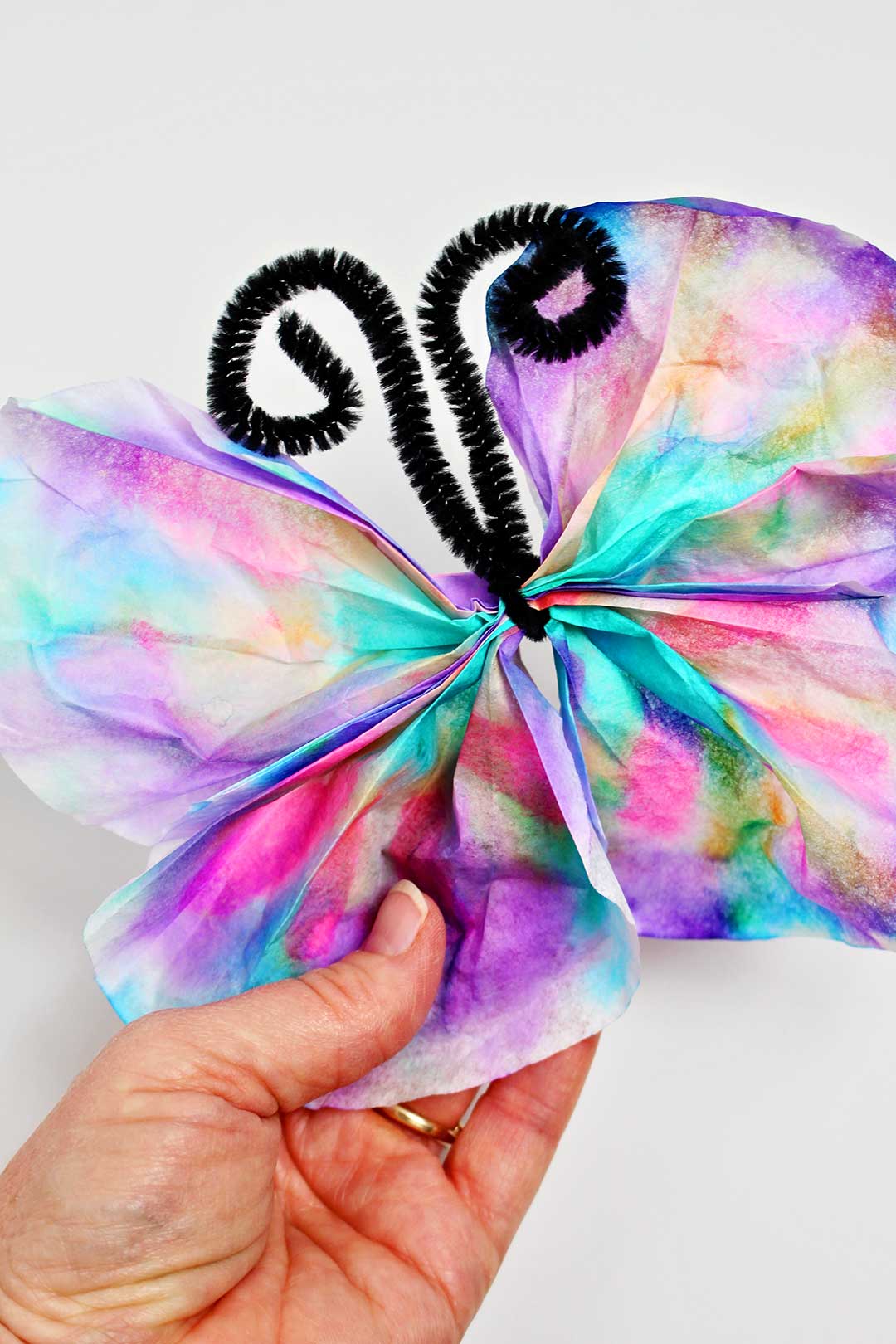 A colorful Coffee Filter Butterfly with a black pipe cleaner for antenna.