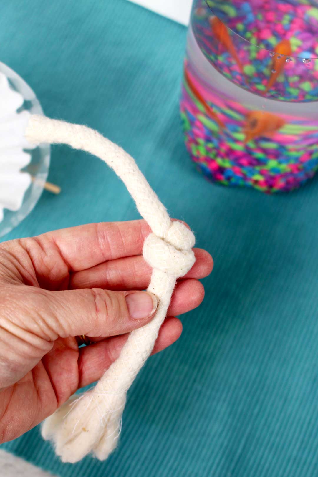 Hand holding cloth rope showing knot next to DIY fish tank and fish.