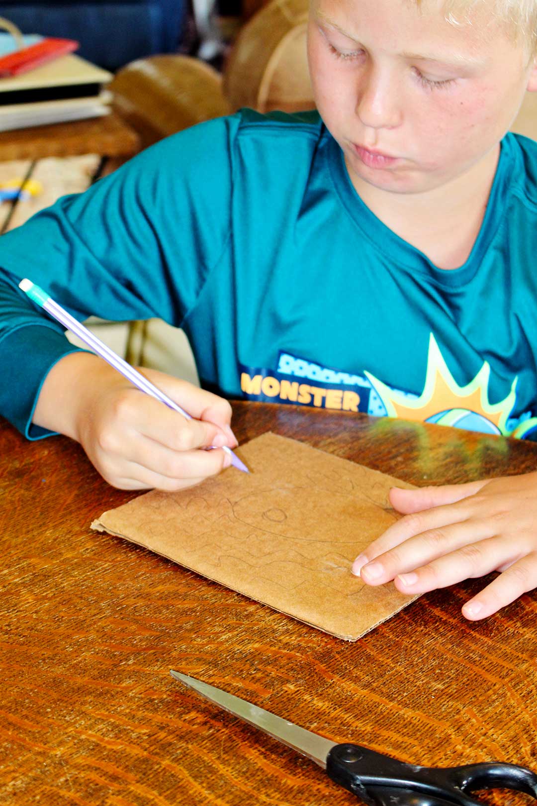 A child drawing a picture of a fish in the water on a piece of cardboard.