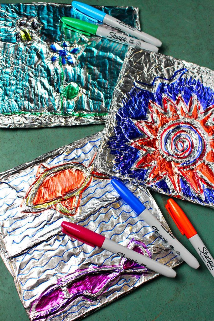 Sharpie markers laying on three colorful Aluminum Foil Embossed Art projects.