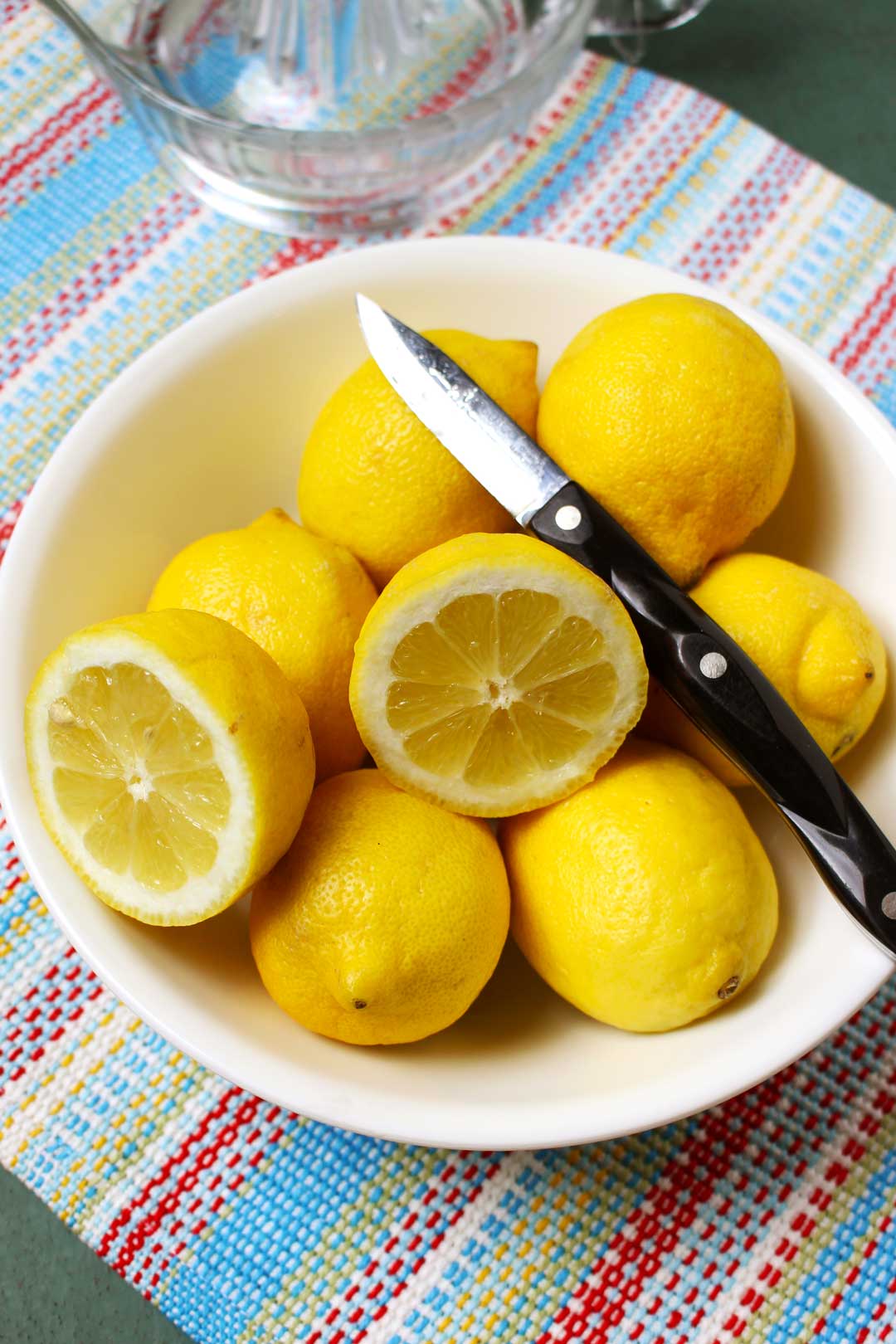 A bowl of lemons and lemon halves with a knife near a glass juicer.