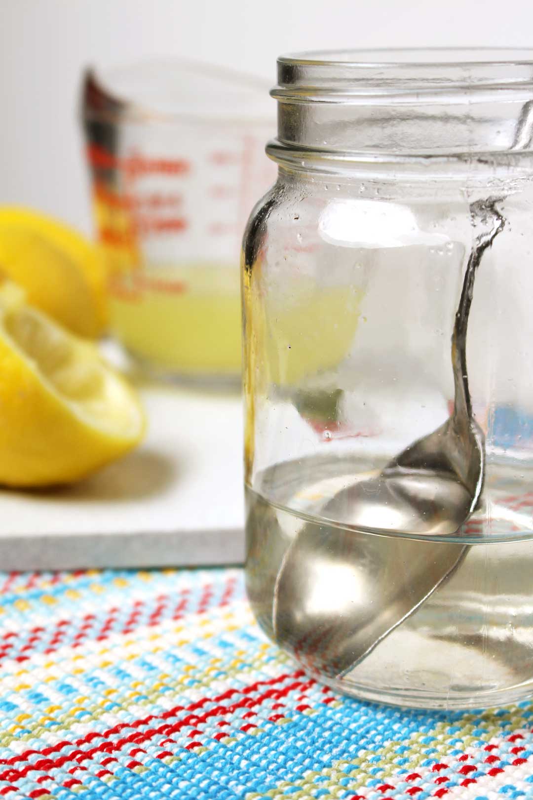 Simple syrup stirred together in a mason jar with a spoon near some squeezed lemons.
