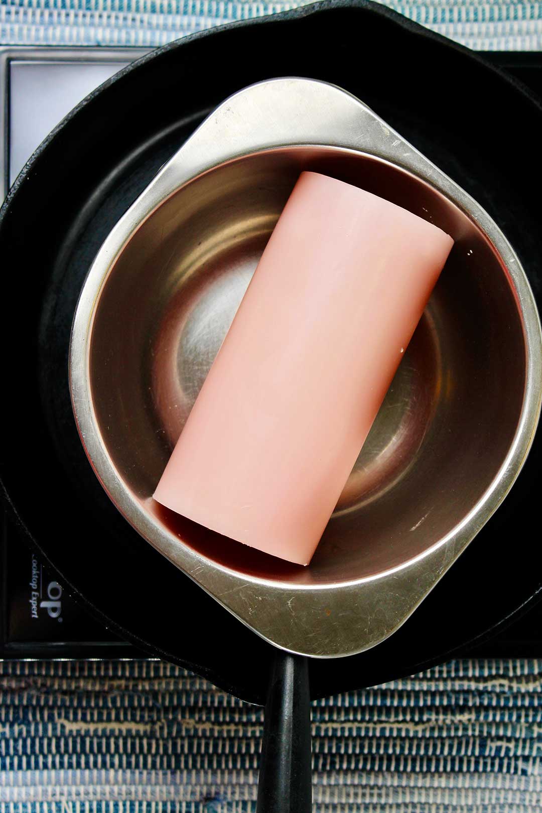 Large pink candle in metal bowl in cast iron pan.