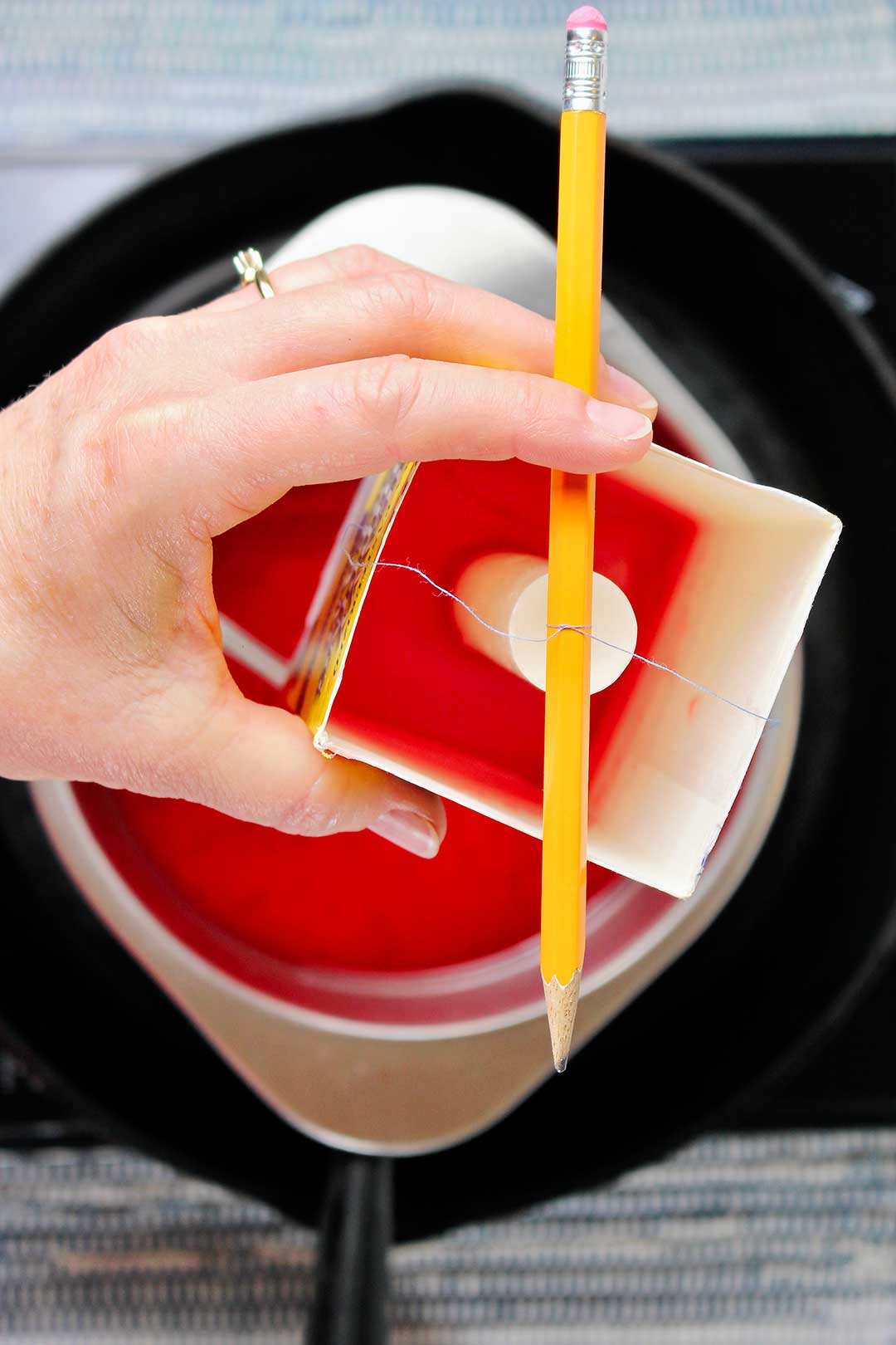 Person holding carton with melted wax inside with pencil holding wick in place.