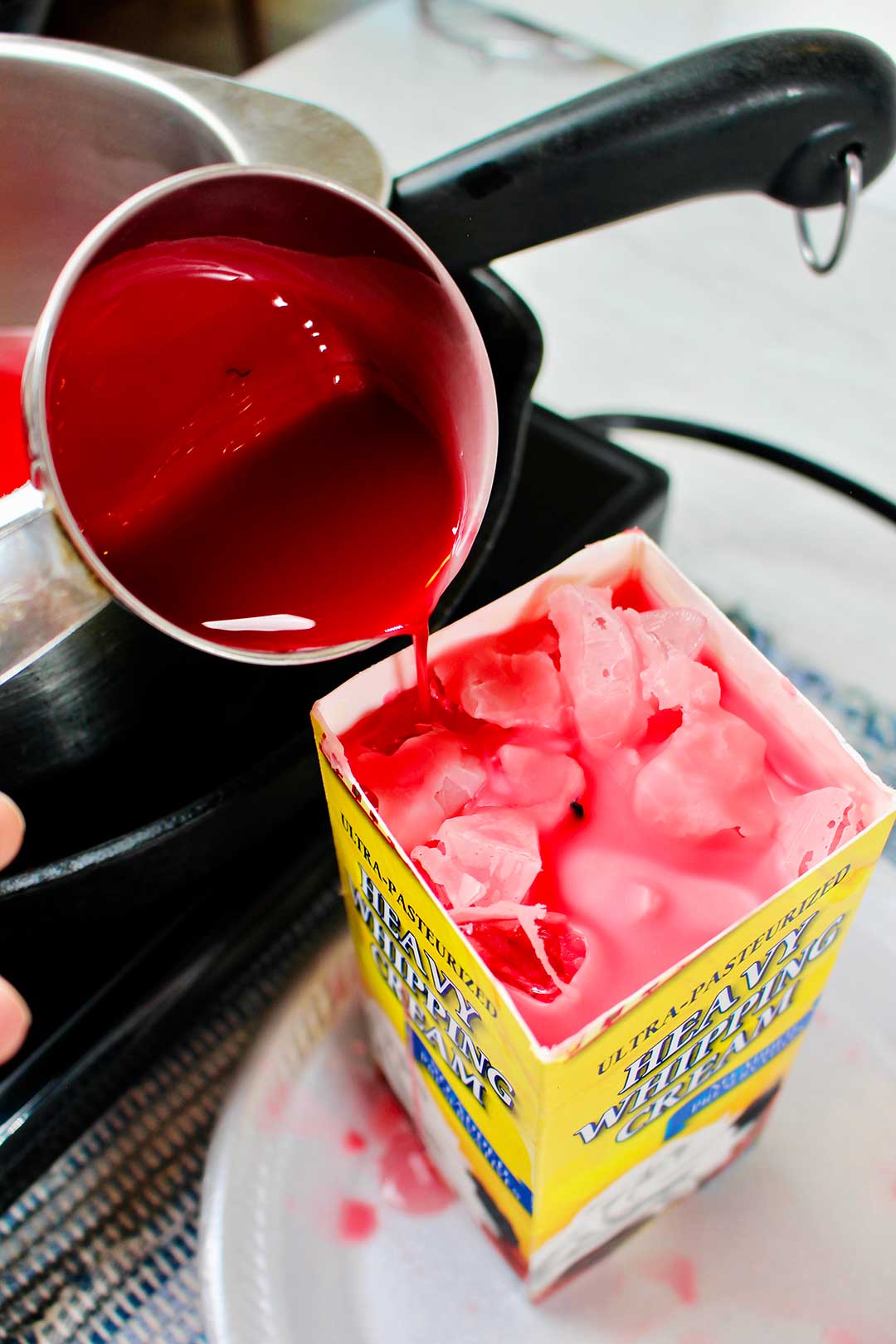 Melted red wax being poured into carton with ice cubes and wick.