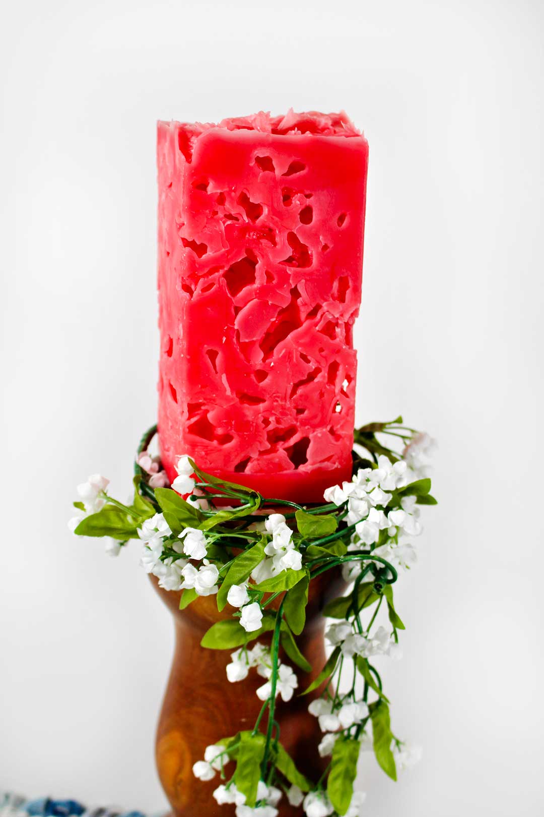 Red rectangular candle on candle holder with greenery and white flowers around it.