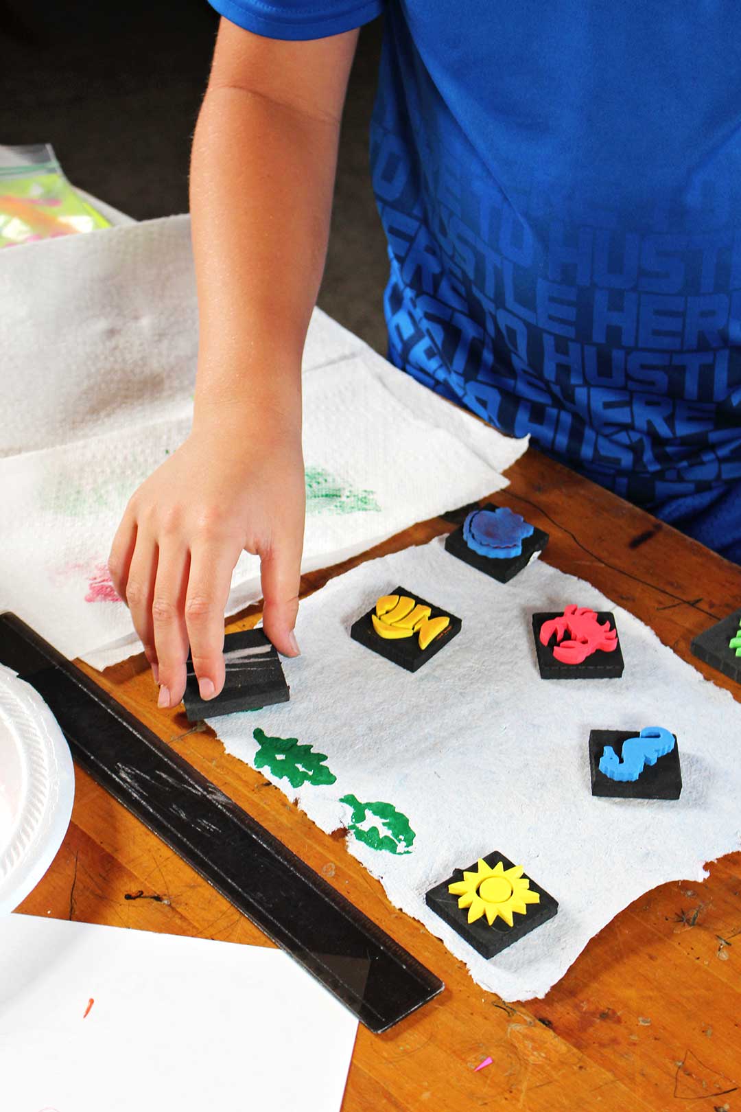 Child in blue shirt stamping shapes on homemade paper.