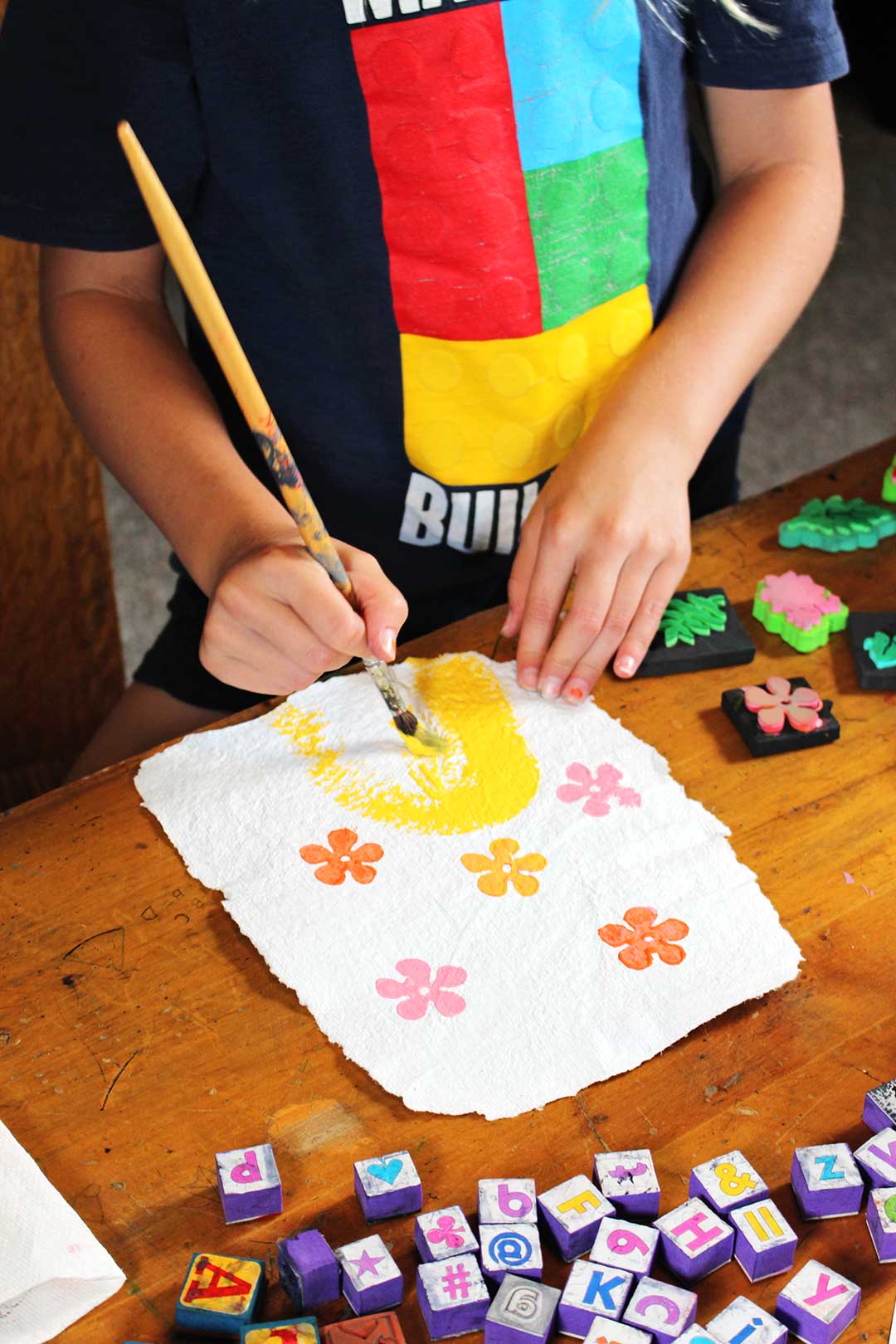 Child painting yellow arch on homemade paper stamped with pink and orange flowers.