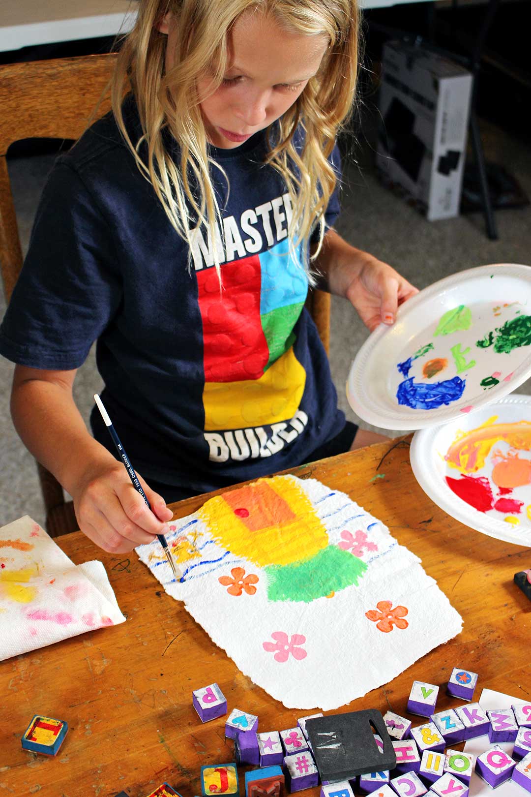 Blond child painting water ripples on homemade paper holding plate of paint.