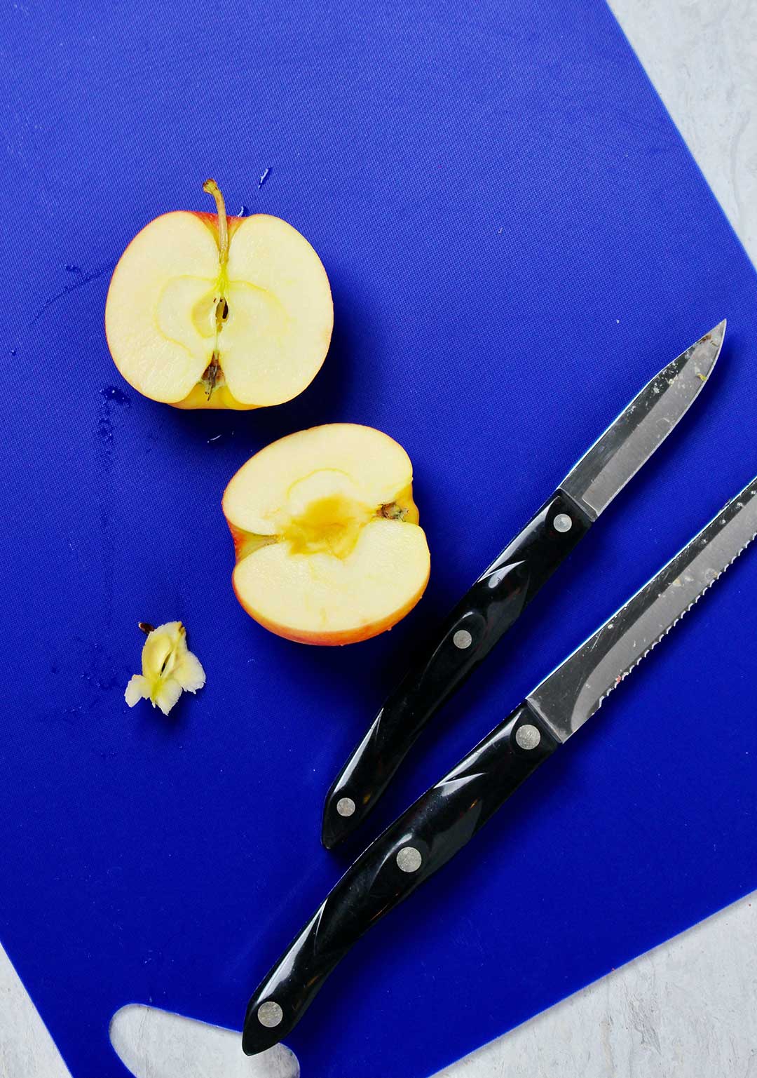 Halved apple with two knives on a blue cutting board.