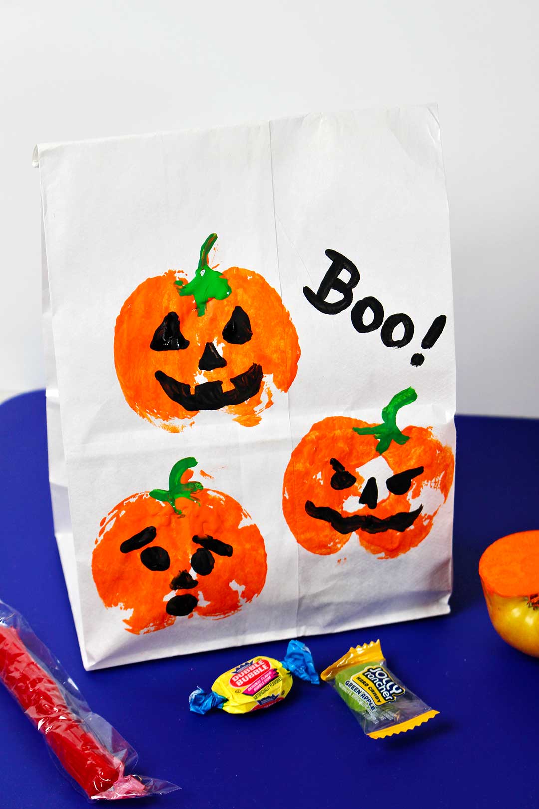 Treat bag with pumpkin prints sitting upright with candy next to it.