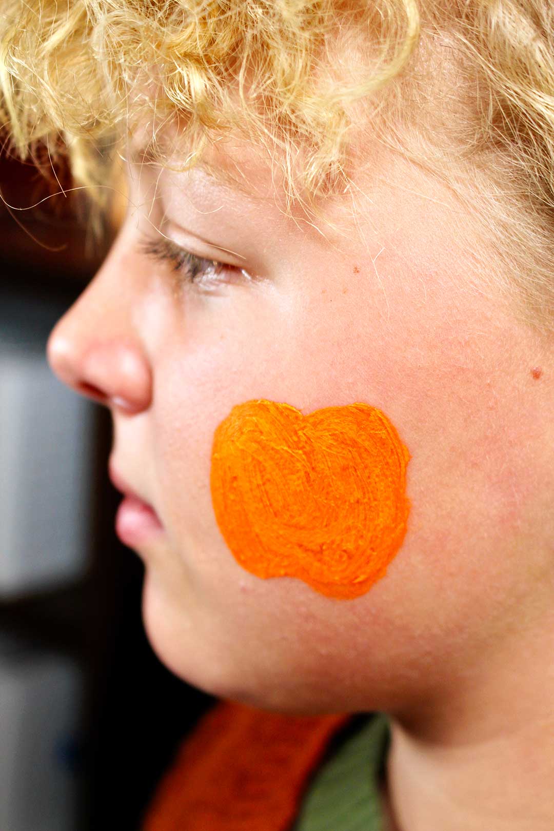 Profile of girls face with orange face paint outline of a pumpkin on cheek.