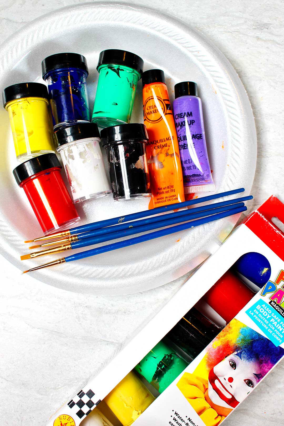 White plate with containers of colored paints and paint brushes near by.