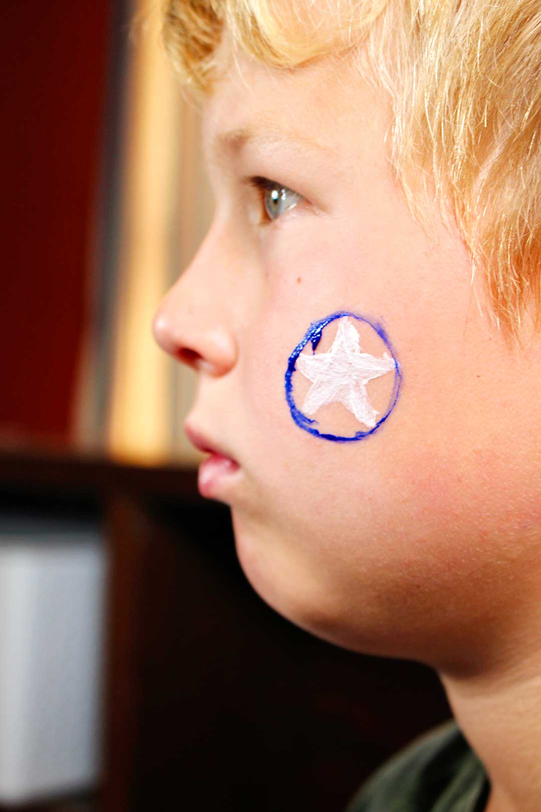 Profile of boy with white star and blue circle around it painted on cheek.