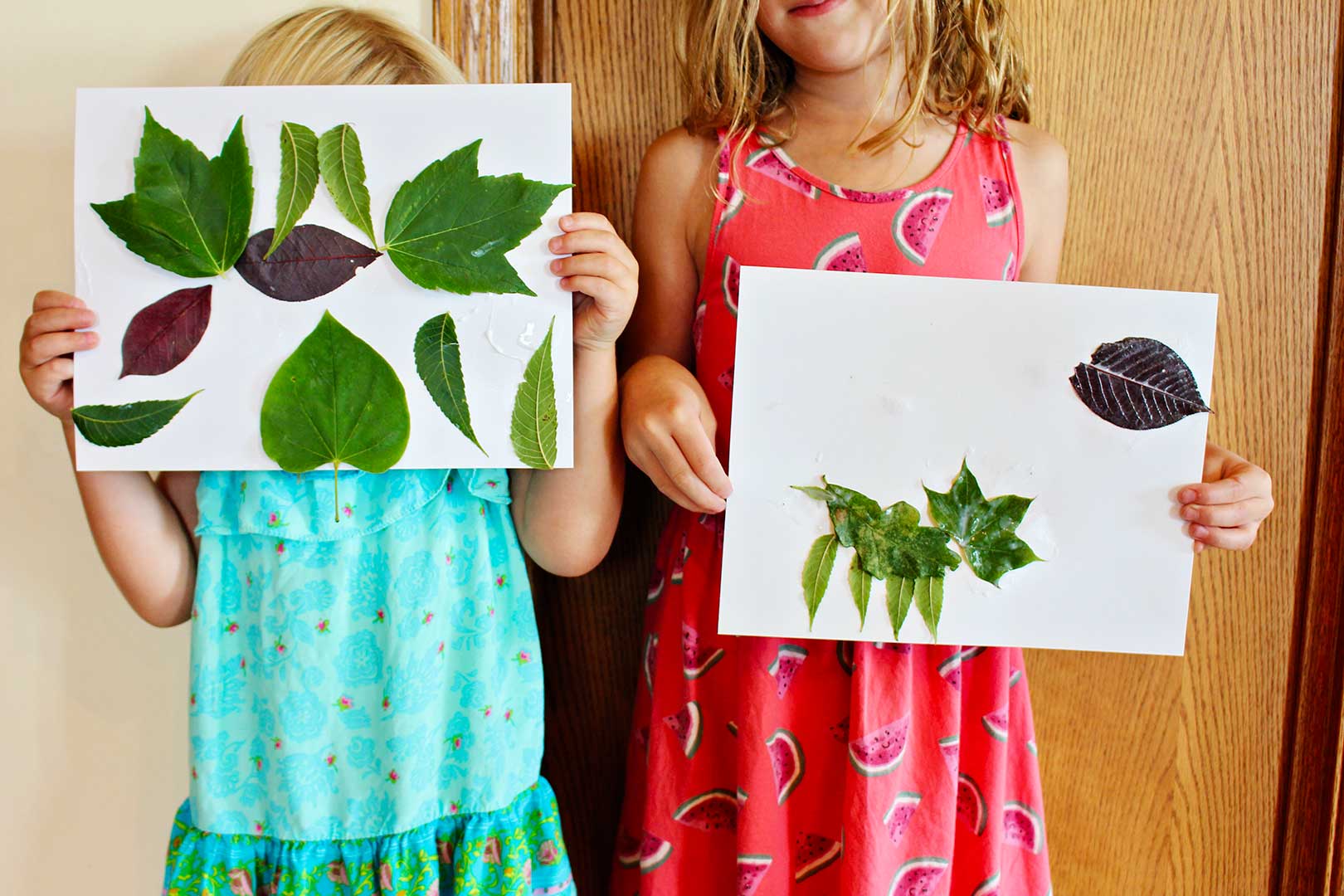Two girls standing side by side showing the camera their leaf collage.
