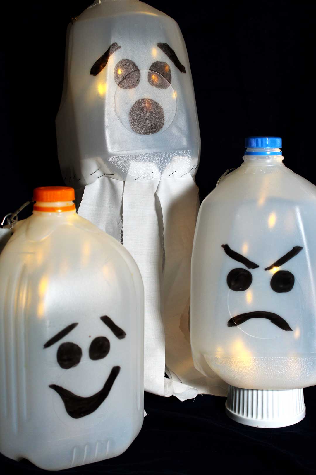 Recycled milk jugs with faces drawn on them to create glowing ghost luminaries.