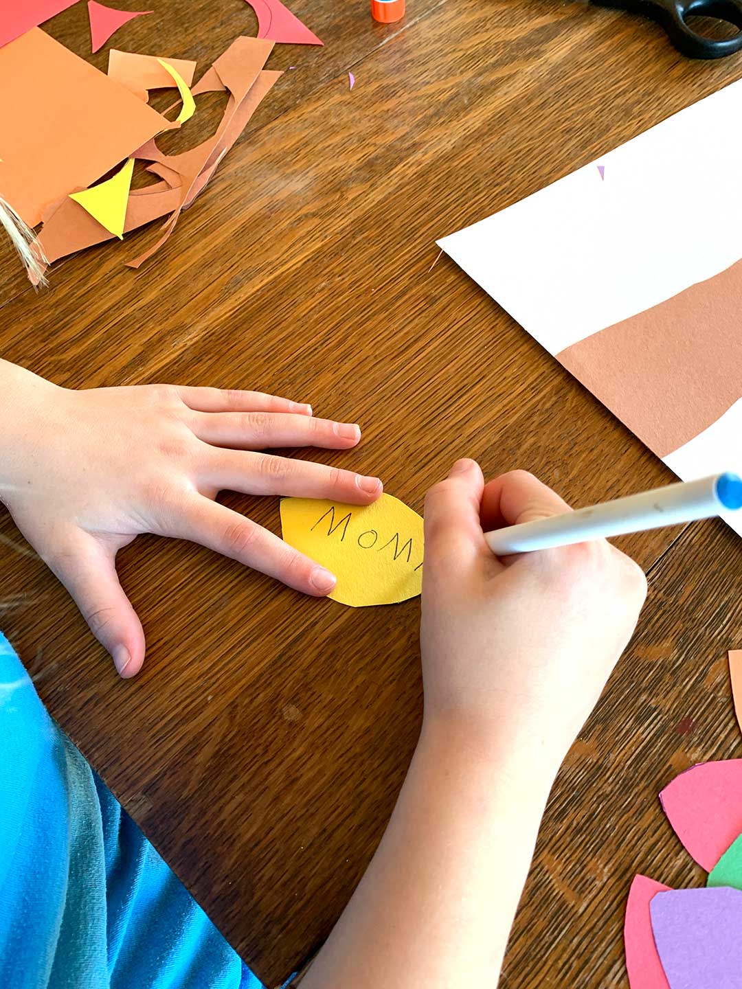 Child writing "Mom" on a yellow thankfulness leaf for their blessing tree.