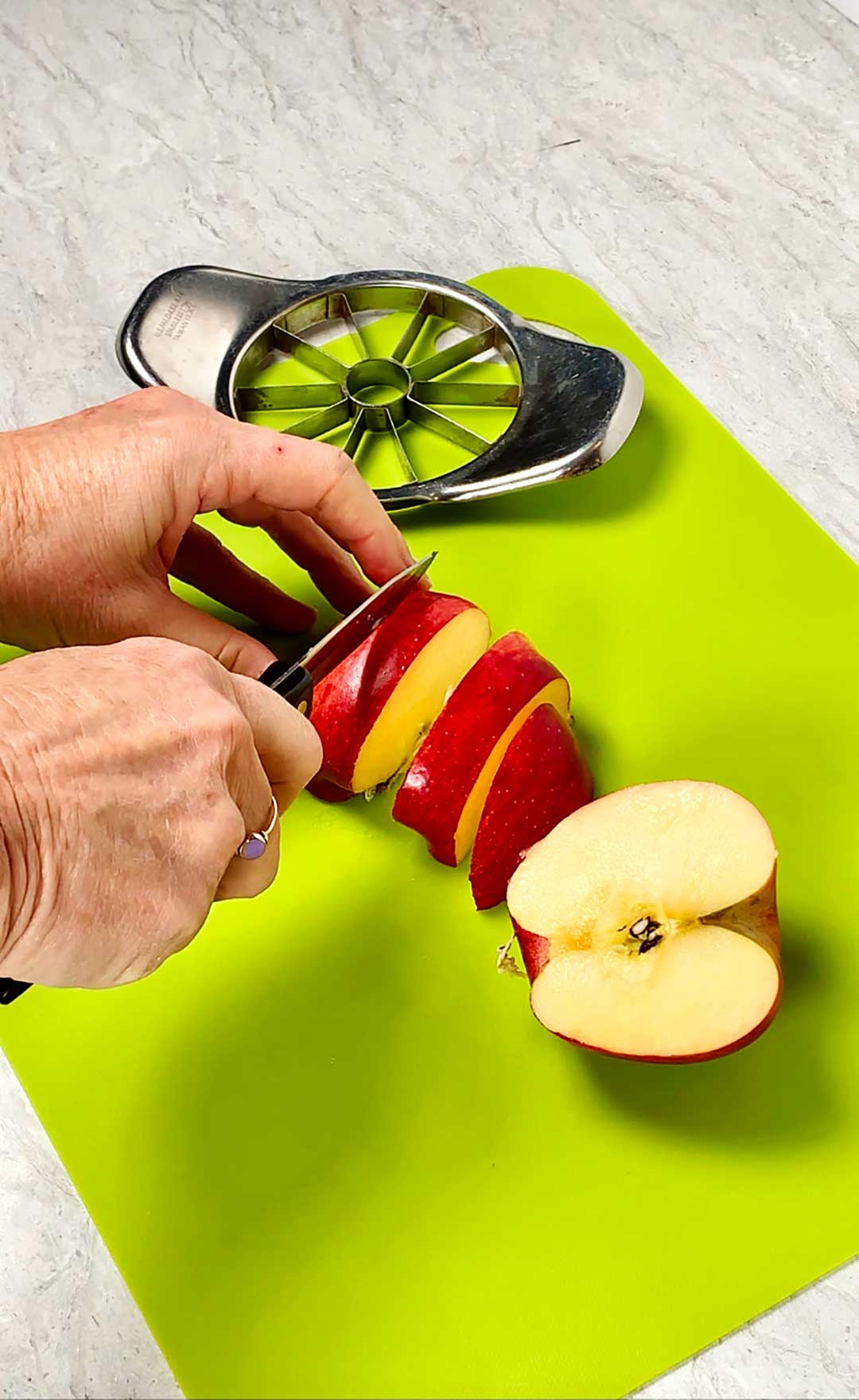 Person slicing apples with a knife on bright green cutting board.